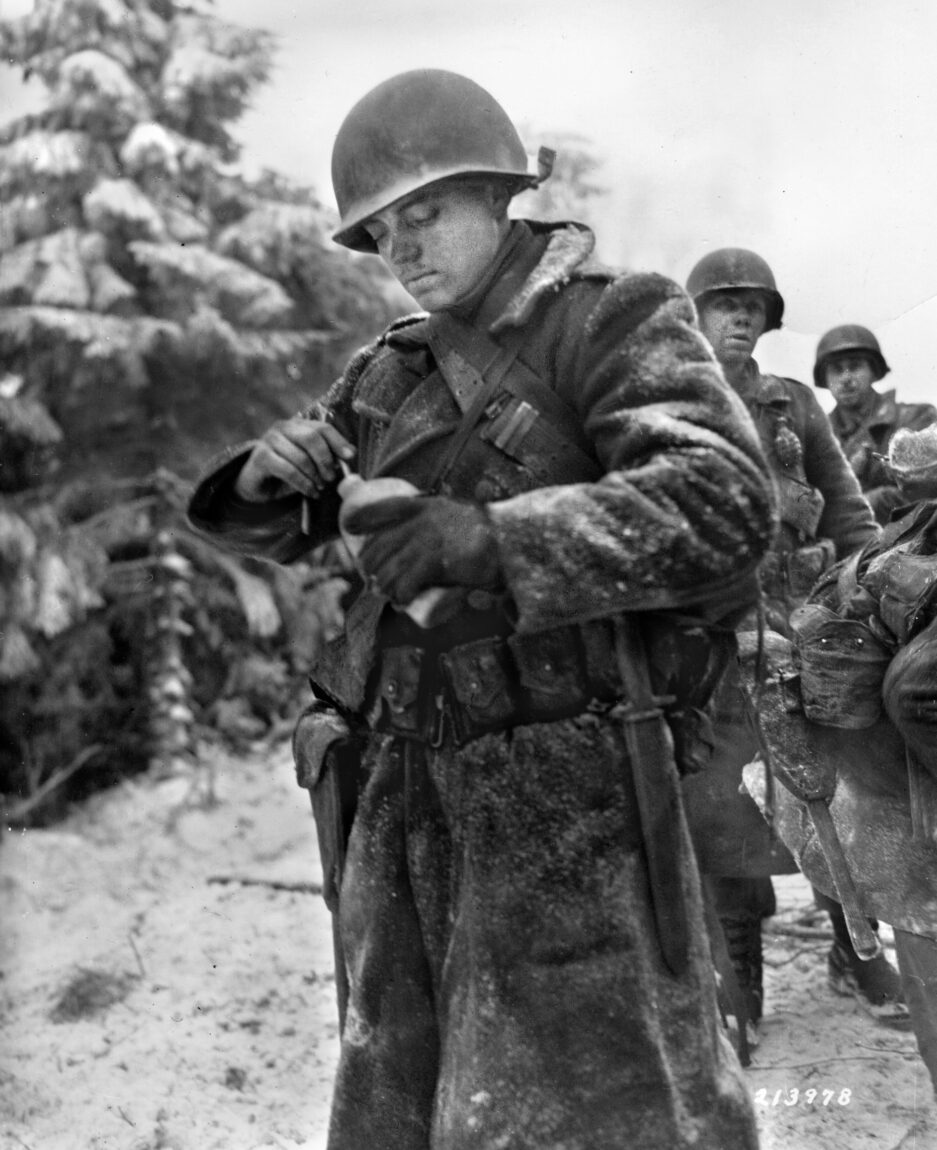 In this photo taken January 8, 1945, soldiers of the U.S. 83rd Infantry Division pause after coming off the front line during the Battle of the Bulge. In the foreground, Private David Hibbitt digs ice out of his canteen so that he can fill it with much needed water.