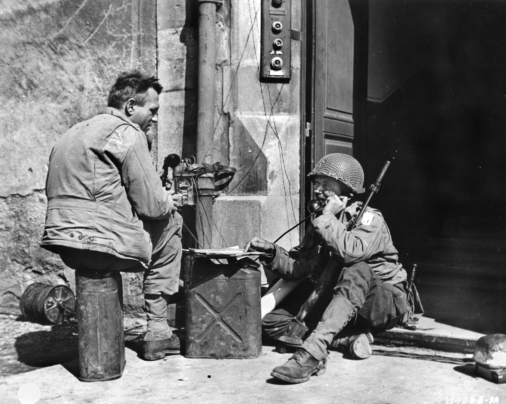 Situated in a doorway somewhere in France, a soldier operates mobile communications gear so that an officer can coordinate mortar fire during offensive operations. As a qualified lineman, Frank Fauver estimates he laid thousands of miles of communication wire for the Army.