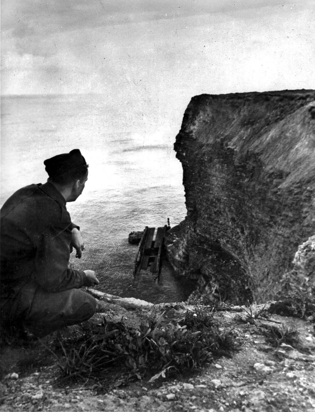 A Stars & Stripes reporter views a wrecked treadway section of a Mulberry artificial harbor marooned below the cliffs of Pointe du Hoc, scene of U.S. Rangers’ heroics.