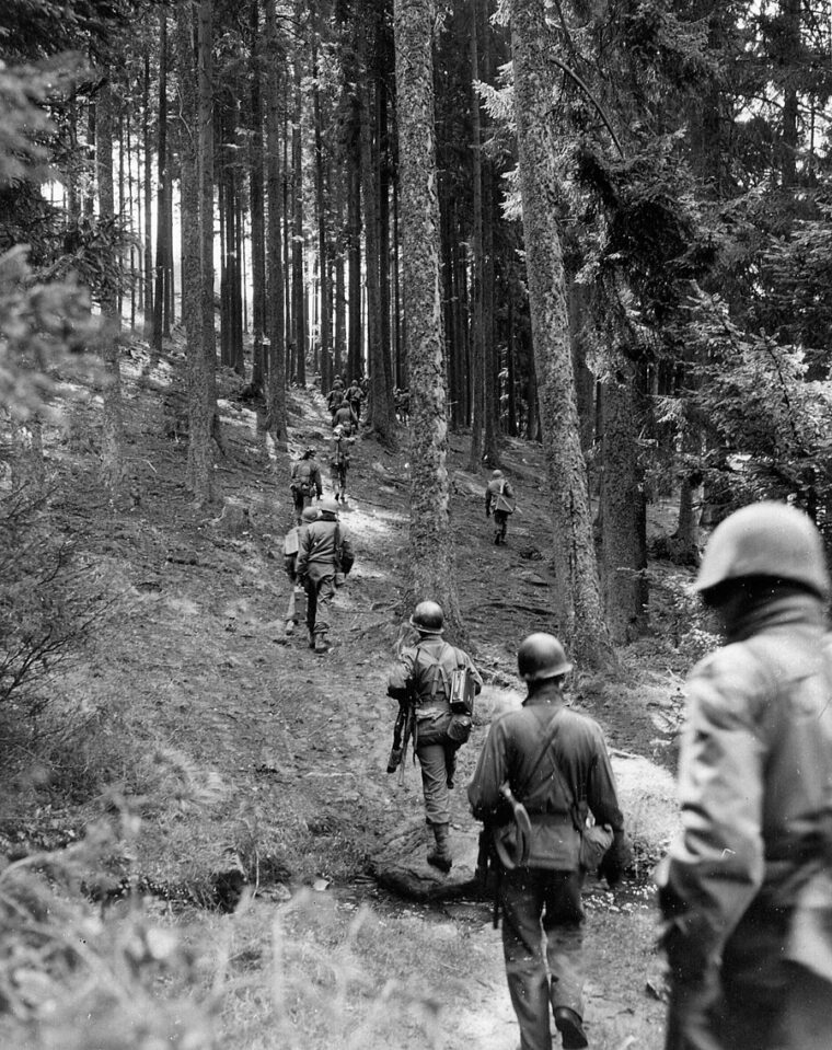 Troops of the 90th Infantry Division move through the woodlands of Czechoslovakia while probing German positions near the southern German-Czech border.