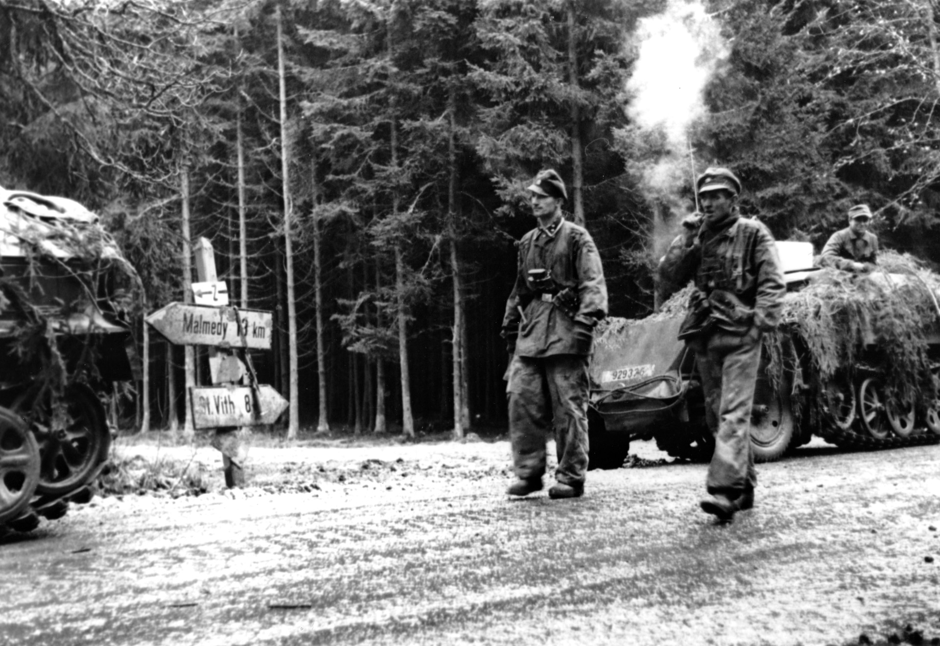 Smoke from his cigar curls upward as an SS officer and his detachment pause at a road sign directing traffic toward the village of Malmedy, Belgium, during the opening hours of the German Ardennes offensive that came to be known as the Battle of the Bulge. In a field near Malmedy, troops under the command of SS Colonel Jochen Peiper committed one of the most infamous battlefield atrocities of World War II.