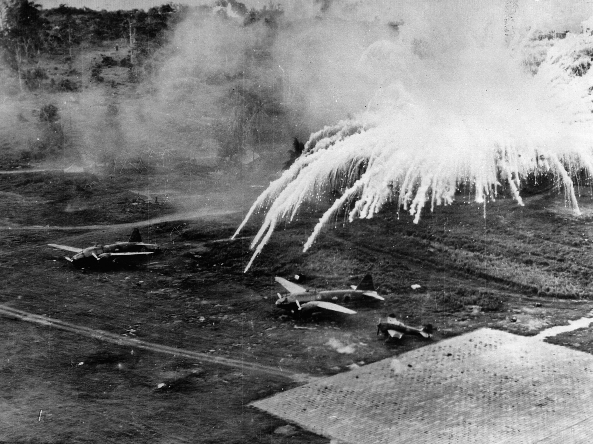 Explosions rock a Japanese airfield near Rabaul. U.S. B-25s and P-38s of the 5th Air Force hammered the site in an effort to put the airfield out of commission.