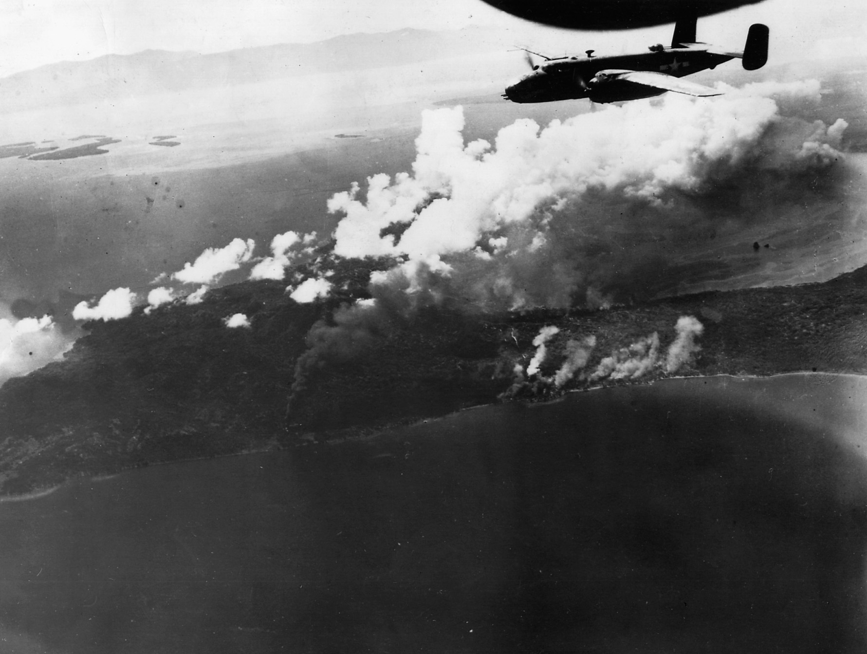 A B-25 Mitchell of the 13th Air Force roars above burning Japanese oil installations in New Britain.