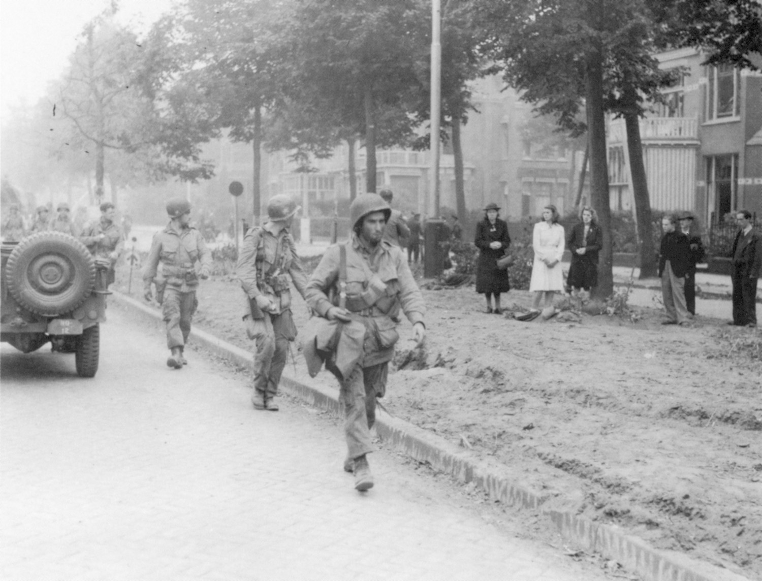 Confused Dutch civilians turn out to watch American soldiers participating in the effort to relieve a battalion of British paratroopers that was isolated at Arnhem and clinging to a futile foothold at the east end of the bridge into the city.