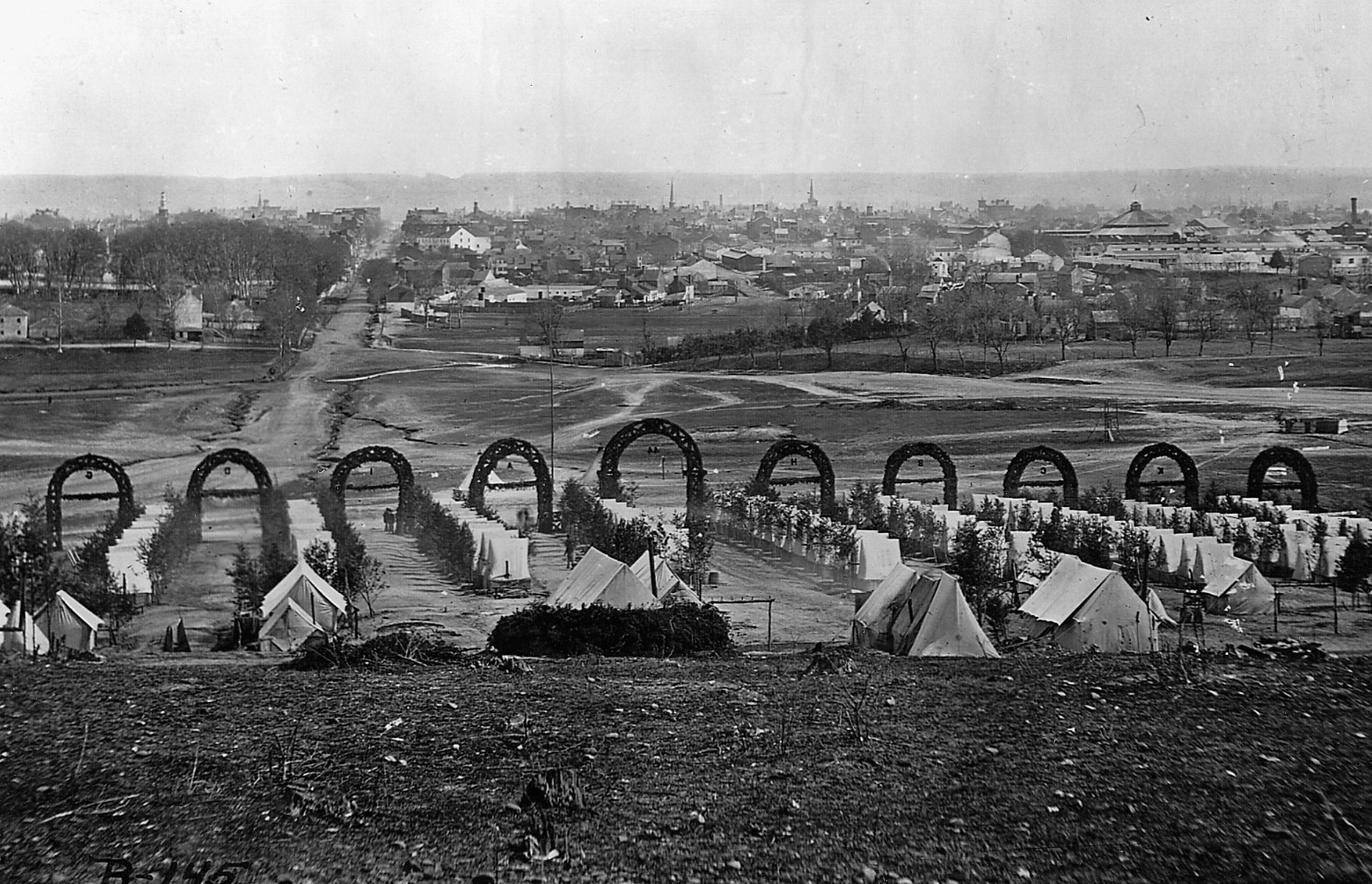 The camp of the 44th New York Infantry Regiment is perfectly laid out on the outskirts of Alexandria, Va. Note the letter for each company on the laurel in front of each unit. Every tent had its own tree and a few had stoves–apparent from the pipes sticking out of their canvas ceilings.