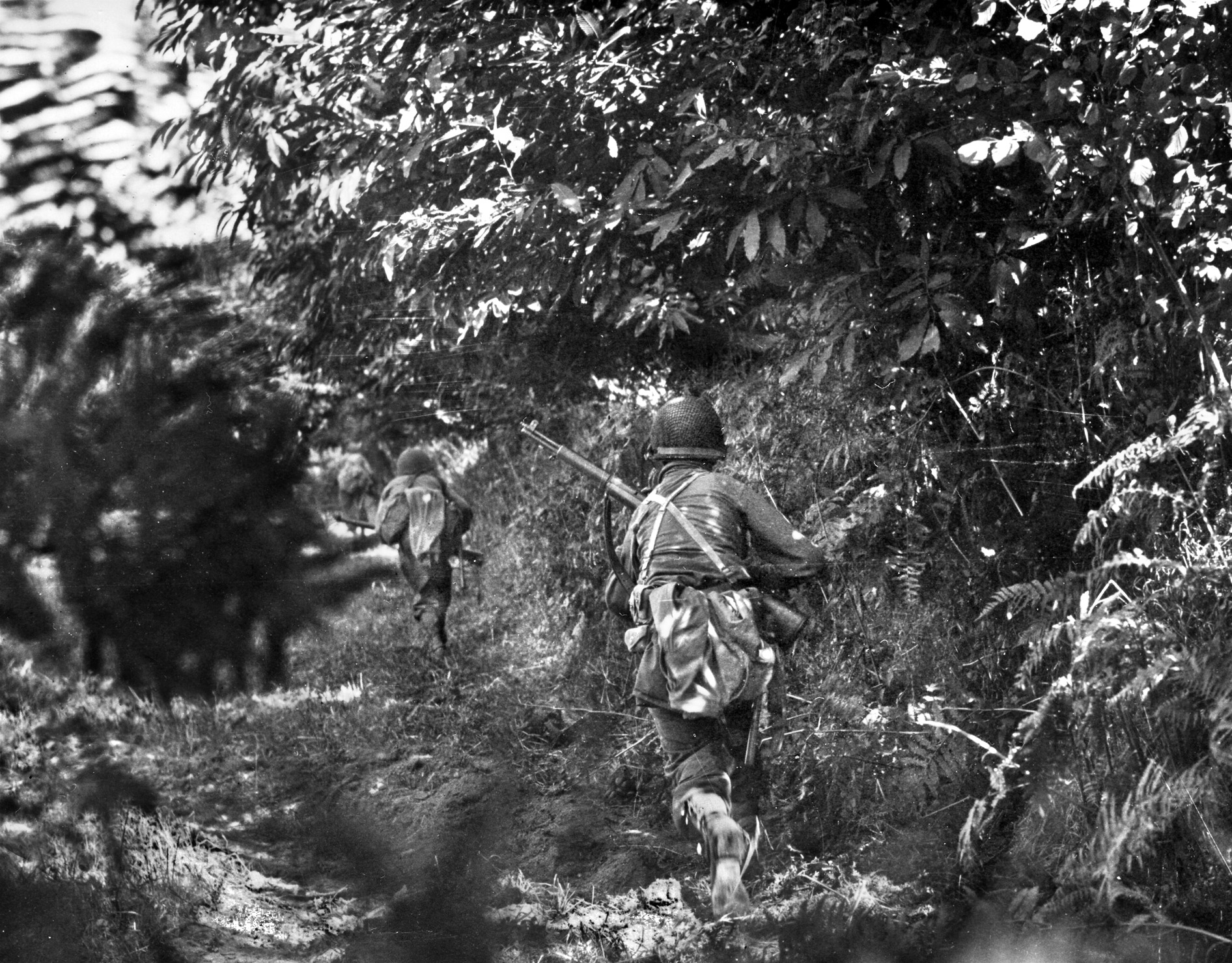 Men of the 30th Division race along a hedgerow to reinforce a new position at Hill 314, August 8, 1944.