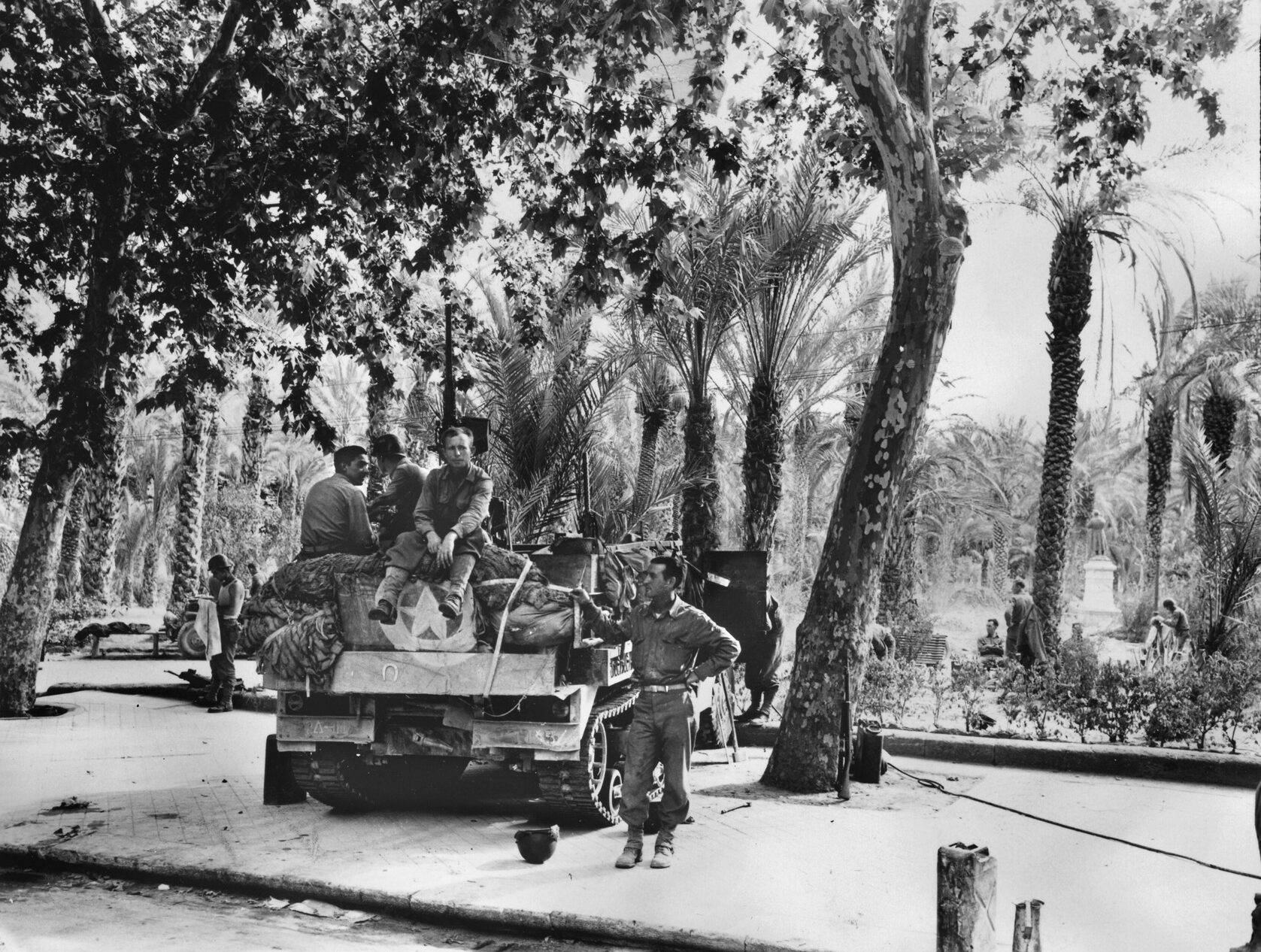 Armored Infantrymen from the 2nd Armored Division take a break in their half-track under the shade of some palm trees.