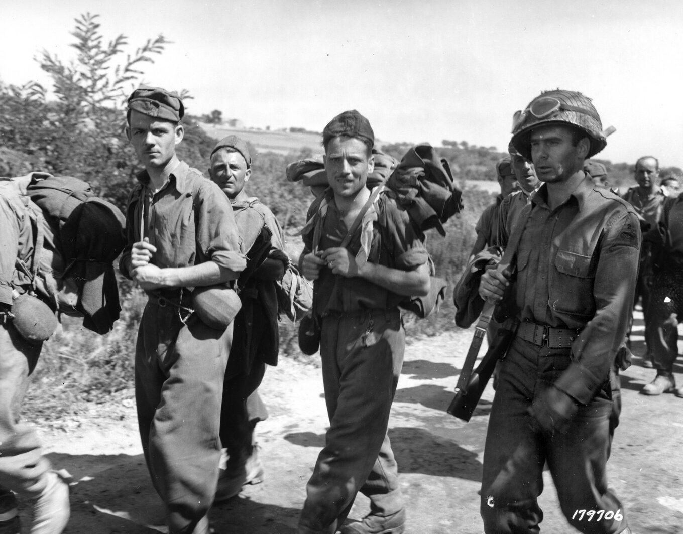 A tanker with the 2nd Armored Division escorts his smiling Italian prisoners to a holding pen.