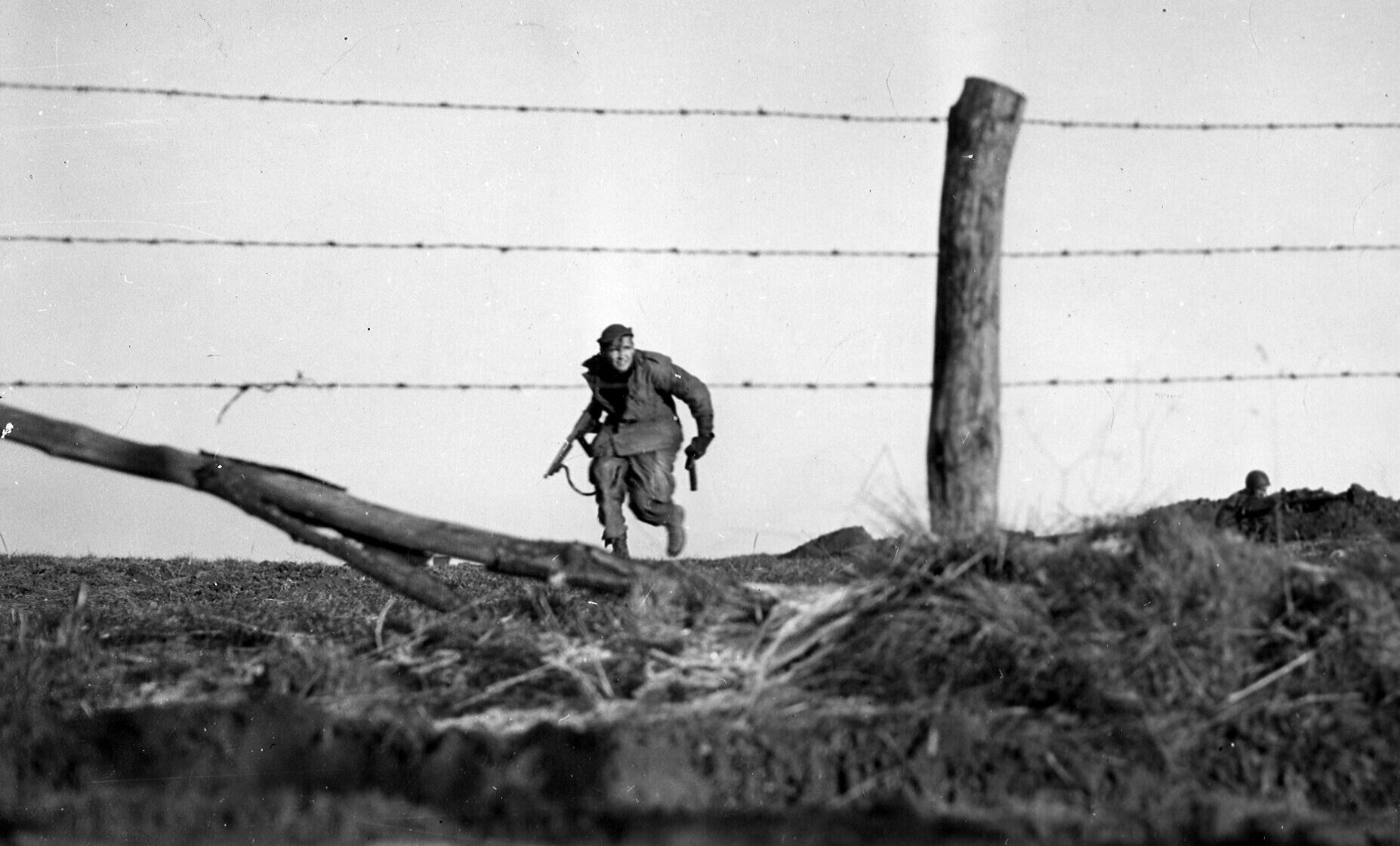 A helmetless American paratrooper from the 82nd Airborne Division carrying a tommygun in full gallop across a Belgian field was captured by the lens of Emil Edgren.