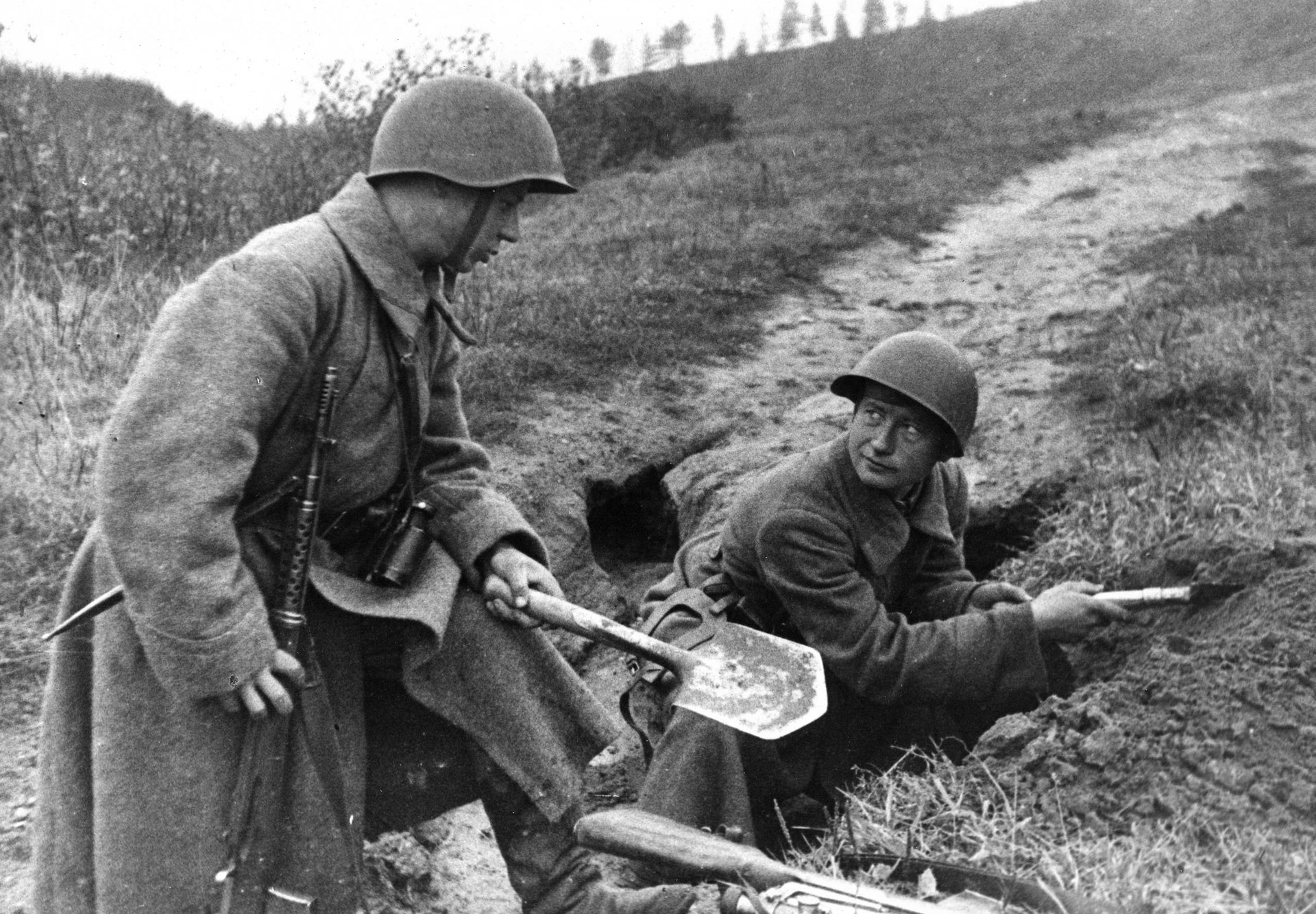 Sergeant Fedor Pekov demonstrates to his pupil, Vladimir Mikheyev, how to dig in and camouflage himself.