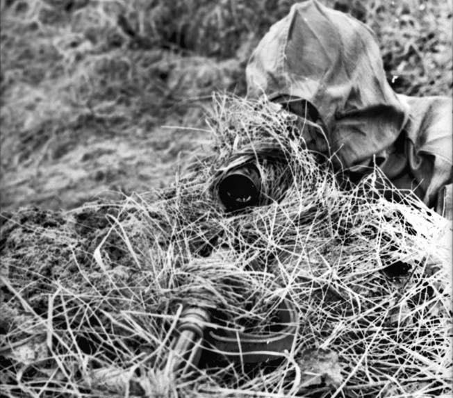 Somewhere in France a well-camouflaged German sniper peers through the scope of his rifle. Sepp Allerberger modified an umbrella to hold brush collected on site to hide his position.