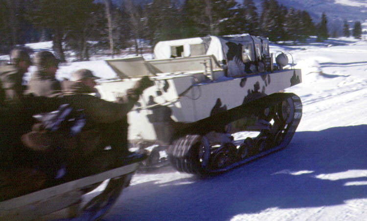 During exercises at Camp Hale, Colorado, in 1943, a camouflaged M-28 cargo carrier speeds along on a snowy landscape while pulling a sled loaded with soldiers of the 10th Mountain Division.