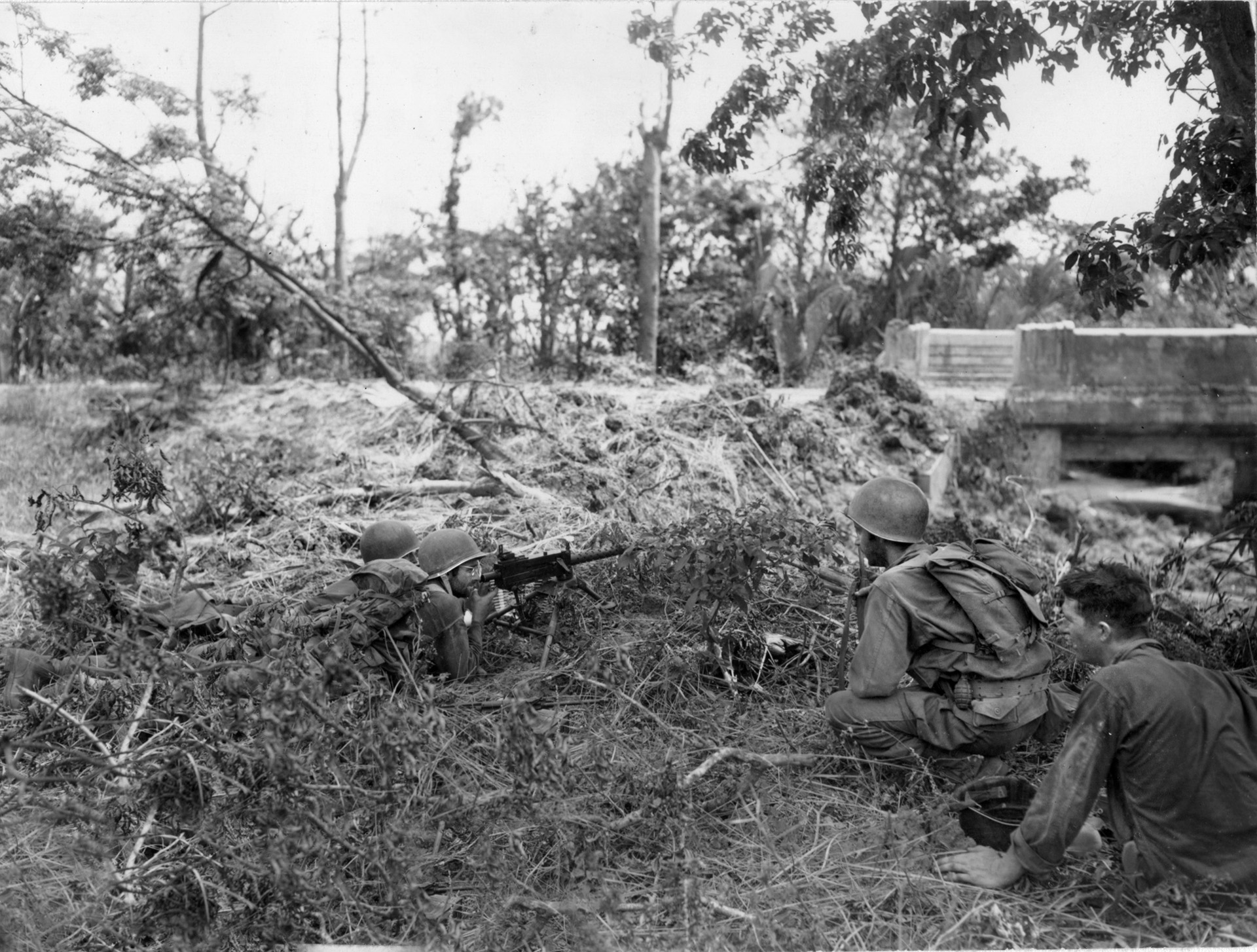 A pair of American soldiers occupy a foxhole with a .30-caliber machine gun at the ready while other members of their squad approach. The sluggish advance against the Japanese on the Bataan Peninsula took its toll on the U.S. troops, while the enemy often fought to the death.