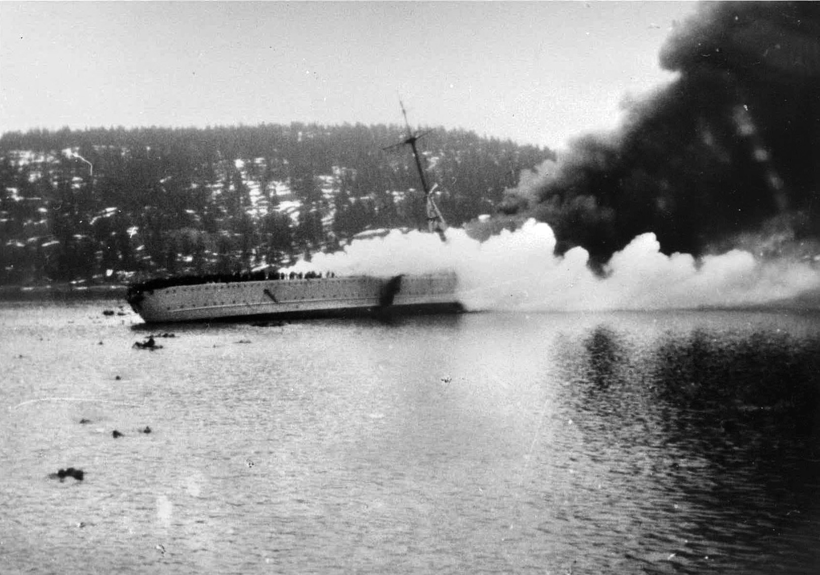 Blücher, hit repeatedly by large-caliber shells and torpedoes from Norwegian shore batteries, lists precipitously to port as smoke billows from its stricken superstructure. 