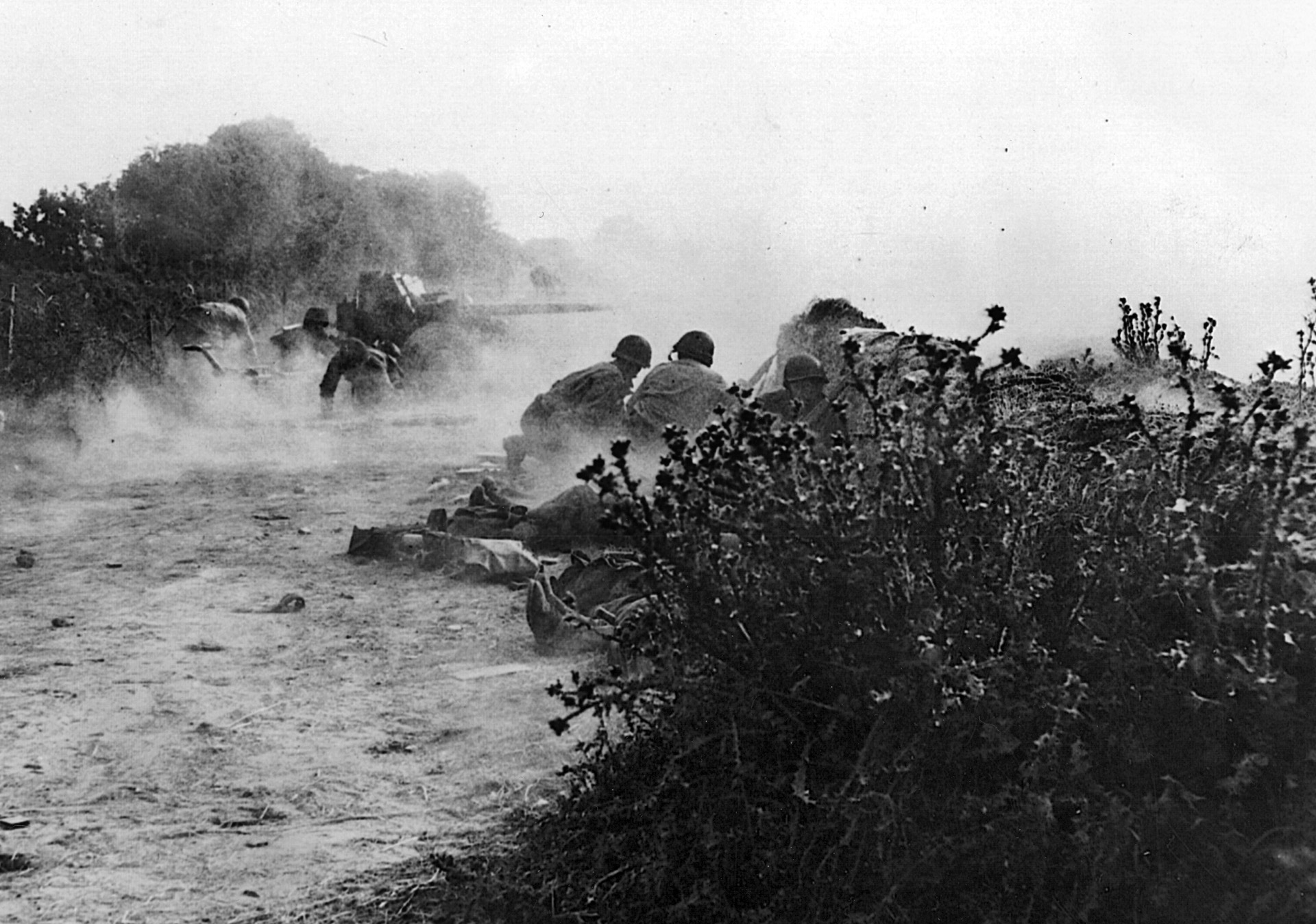As they fight their way toward Cherbourg, advancing painfully along the Cotentin Peninsula, American troops from an antitank unit take cover as German fire peppers around them.