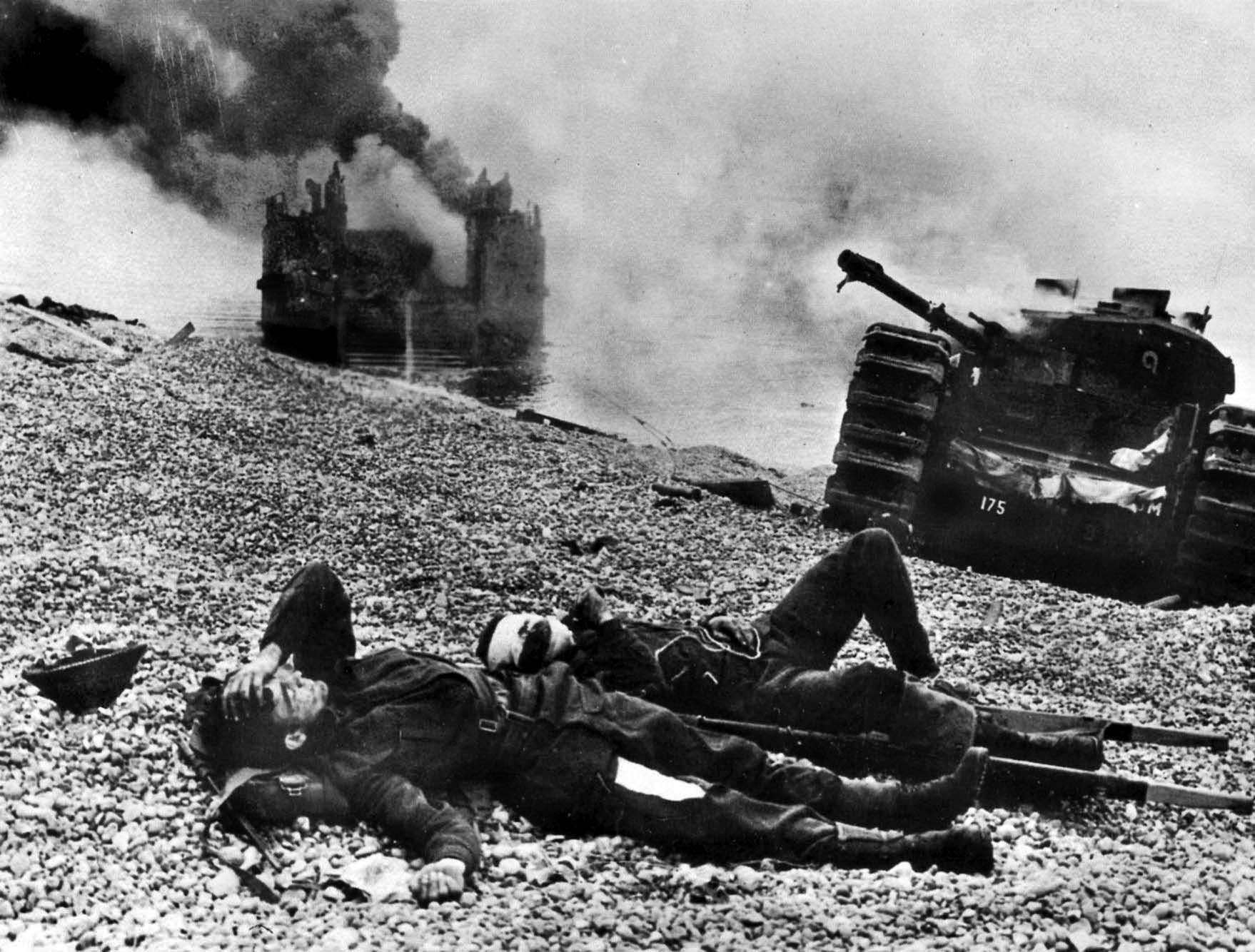 As smoke billows from a destroyed landing craft and tank, wounded Canadian soldiers lie on the beach at the French resort town of Dieppe, scene of an abortive raid against the coast of Nazi-occupied France in August 1942. 