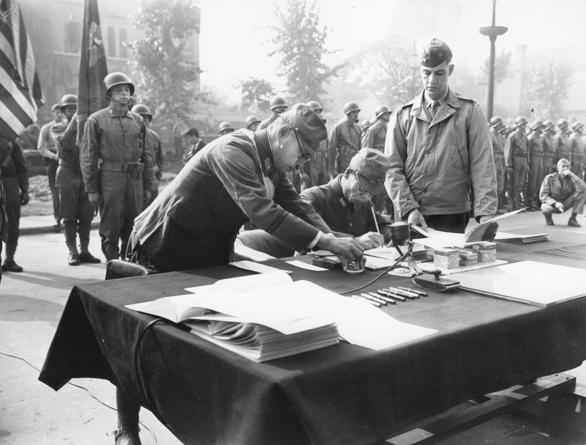 Japanese Maj. Gen. Ginosu Uchida signs surrender documents in the city of Tientsin, China, as World War II comes to an end. General Keller Rockey, commander of the U.S. Marine III Amphibious Corps, watches the proceedings. 