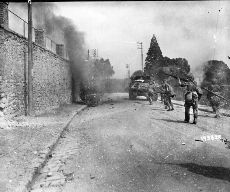 Trailing a tank destroyer down a road, an American soldier raises his M-1 rifle to fire at a German sniper. These soldiers are en route to the Seine River bridge north of Fontainebleau.
