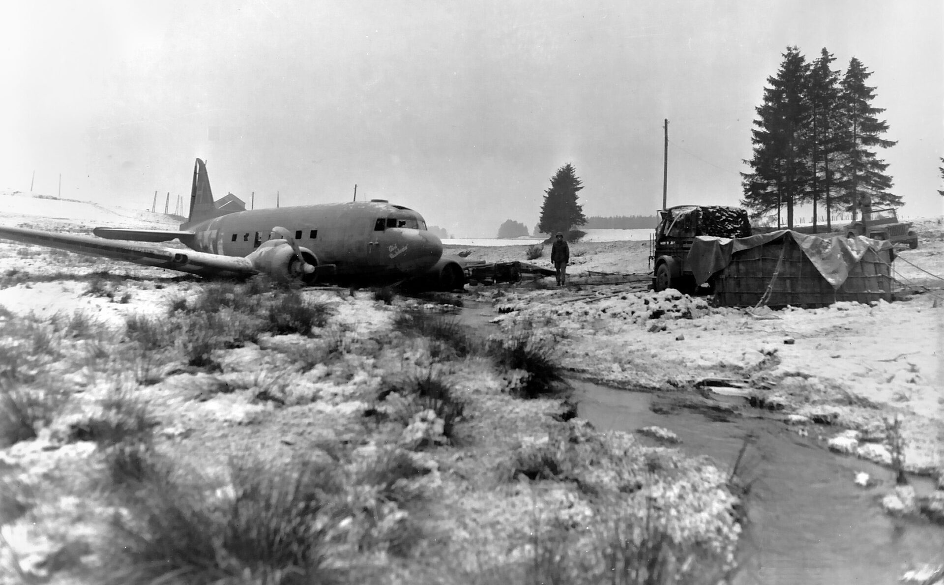 The pilot of a C-47 transport plane crash-landed safely after being shot down during resupply of 101st Airborne units near Bastogne during the Battle of the Bulge.