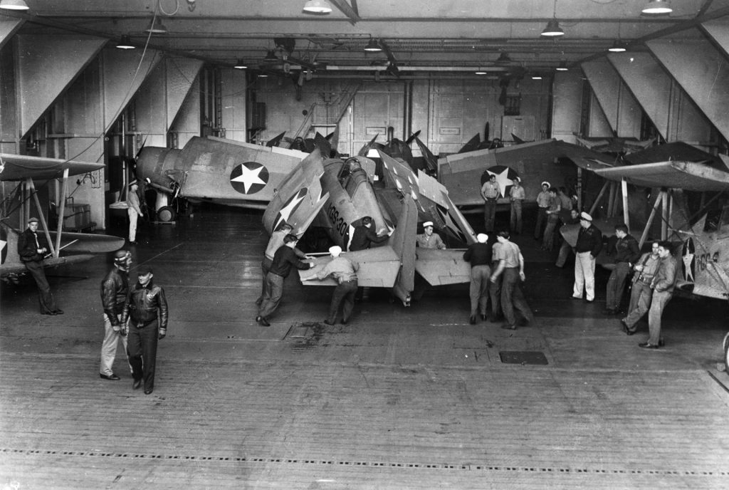 A view of Wildcats being prepped inside the hangar deck of the USS Long Island in June 1942. Curtiss SOC-3A scout-observation planes are visible at right.