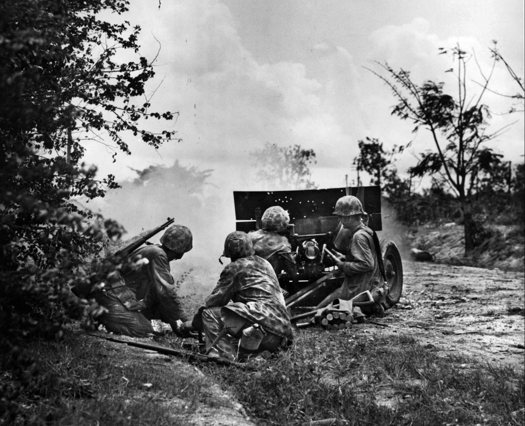  The crew of a 37mm light field gun, its shield perforated by numerous bullet holes, fires at Japanese positions near Garapan.
