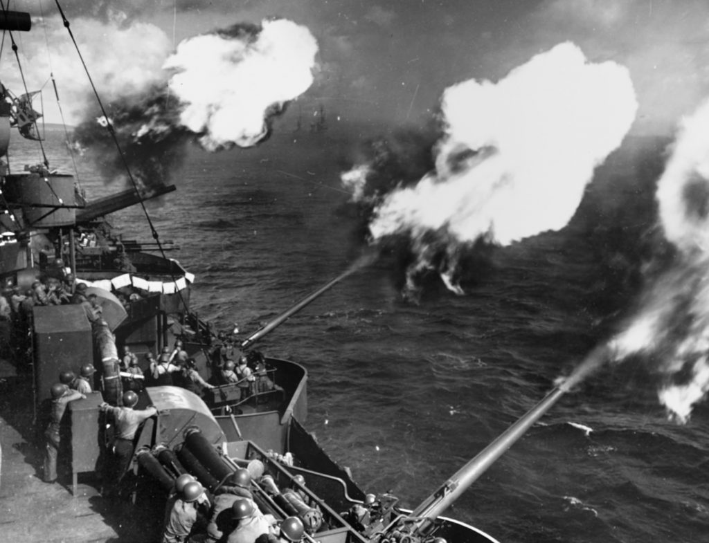 Five-inch guns of the cruiser USS Wichita soften up Japanese targets on Saipan, June 13, 1944. The guns' simultaneous discharge indicates they are firing under director control. 