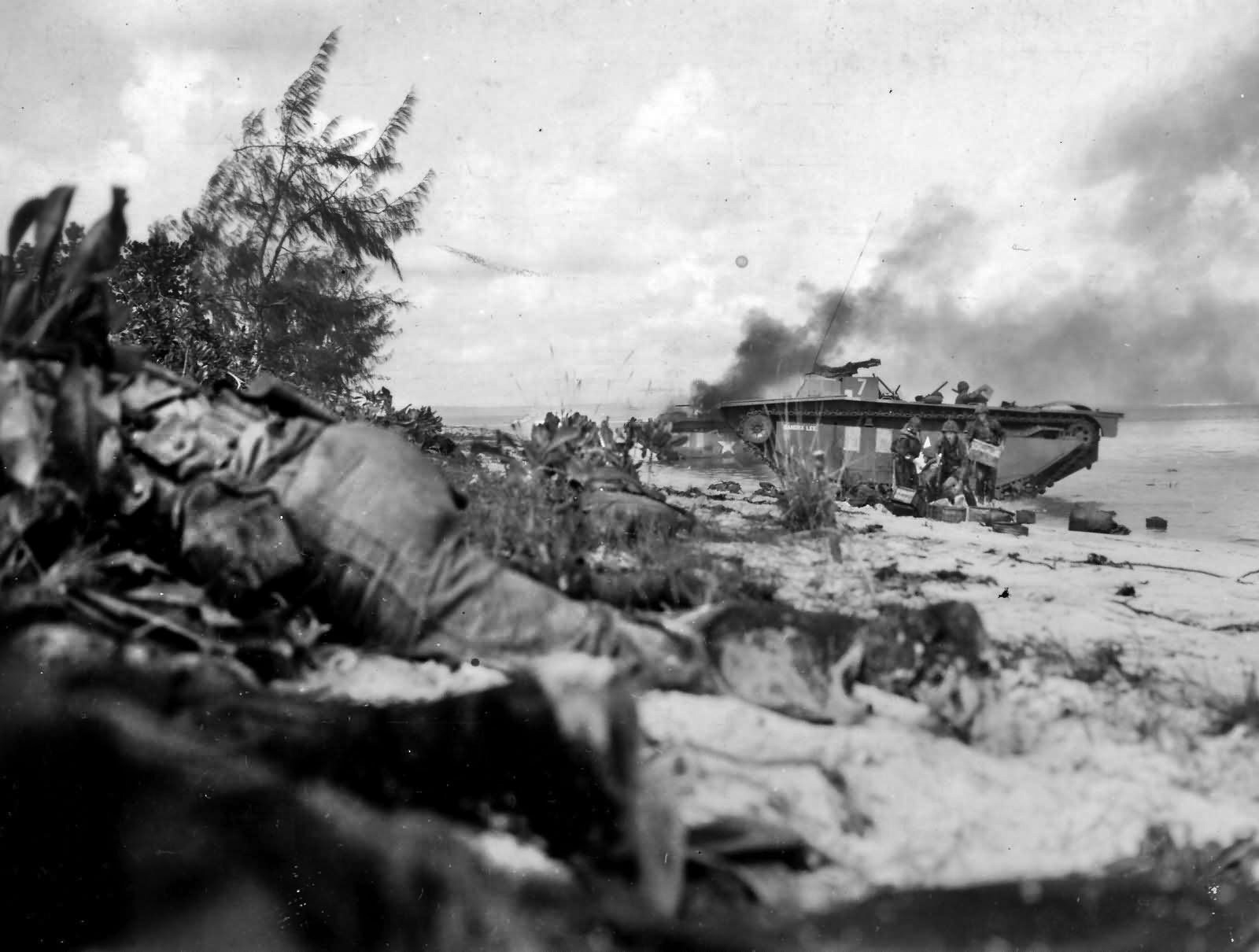 Marines offload medical supplies from an LVT while another landing craft burns in the background. 