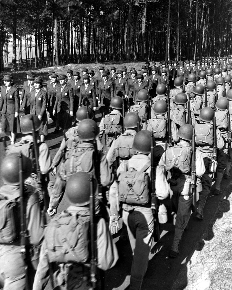 A formation of women Marines, officially known as Marine Reservists, marches smartly past their male counterparts in combat gear at Camp Lejeune, North Carolina, 1943. The Marines Corps was the last branch of service to accept women. 