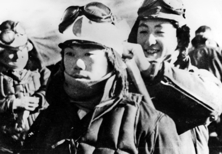 A solemn Kamikaze pilot has his hachimaki headband, symbolizing manly courage, attached by a smiling comrade. Ancient Samuri warriors wore a folded white cloth when going into battle to keep their long hair and sweat out of their eyes.
