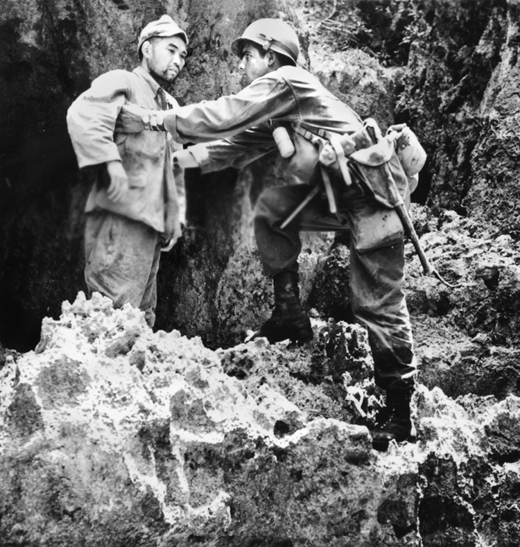 An American soldier checks a surrendering Japanese soldier for hidden weapons. Only about 11,000 Japanese out of a garrison of over 100,000 were taken prisoner by the Americans.