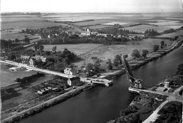 Taken shortly after the war, this photograph depicts the bascule bridge raised over the Orne Canal. The village of Bénouville is at left, with the Café Gondrée closest to the water. The café was turned into an aid station once the bridge was taken.