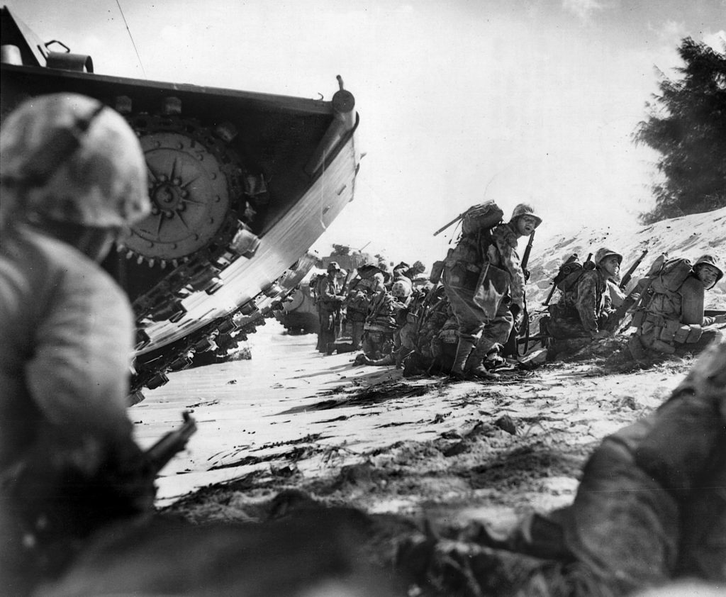 With an LVT behind them, the first wave of U.S. Marines land on the Saipan beachhead on June, 15 1944, while waiting for supporting waves to arrive before moving out to attack Japanese positions. 