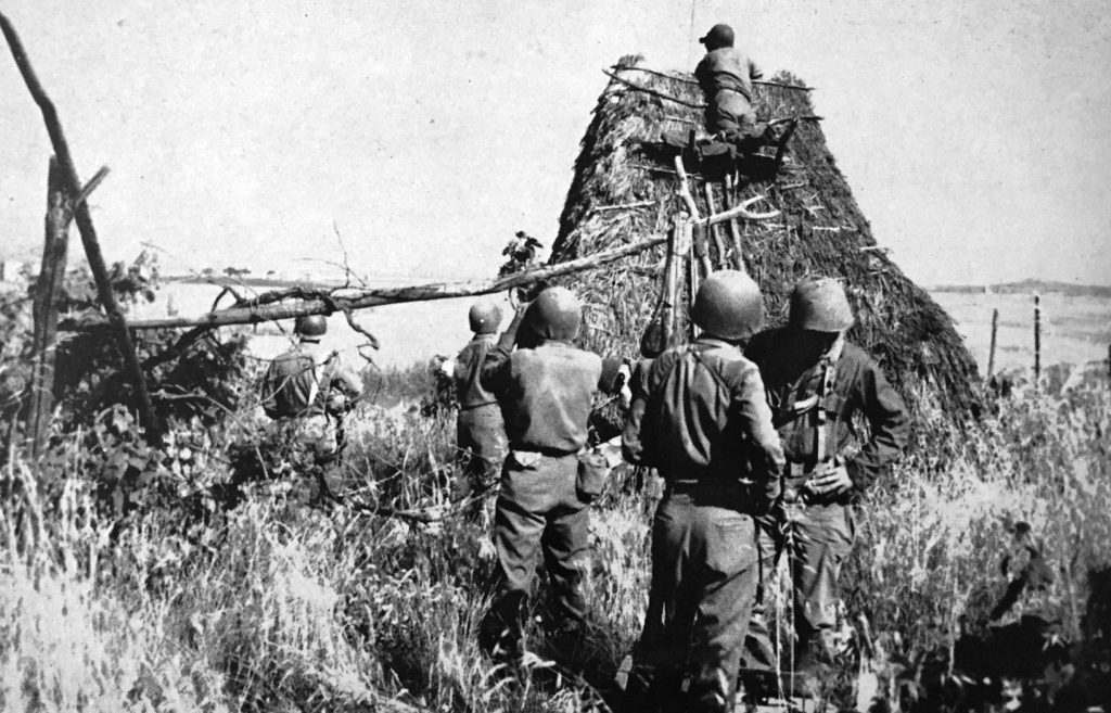 GIs of the 45th Infantry Division use an Italian hayrack as an observation post in a farm field near Anzio. 