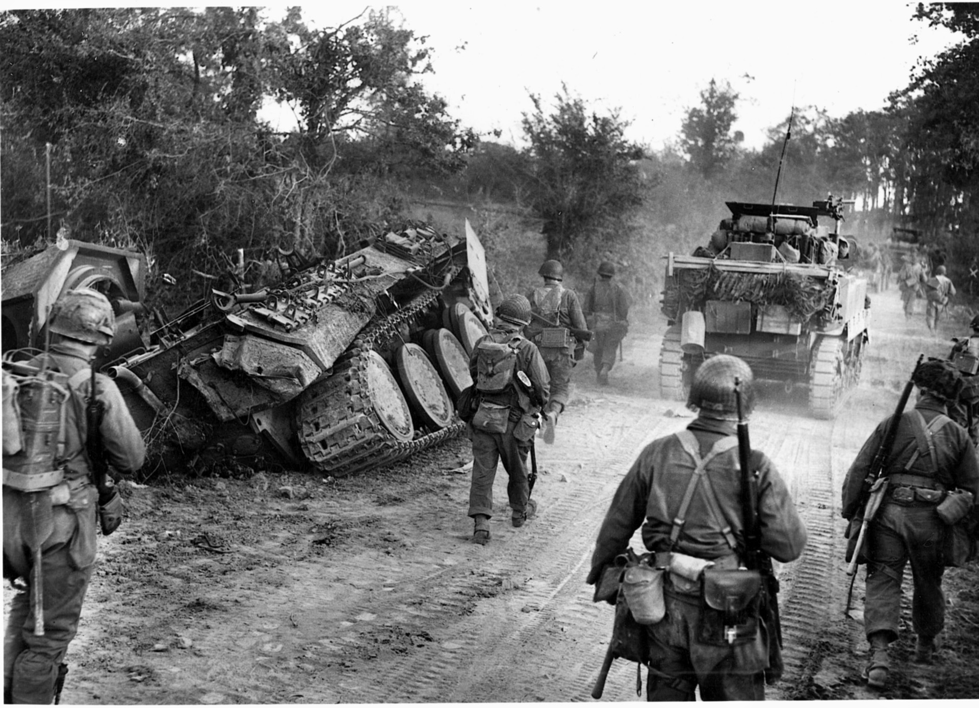 U.S. forces move down a French road littered with German vehicles. The Third Army would advance some 97 miles in the first 10 days of the breakout from St. Lo. 