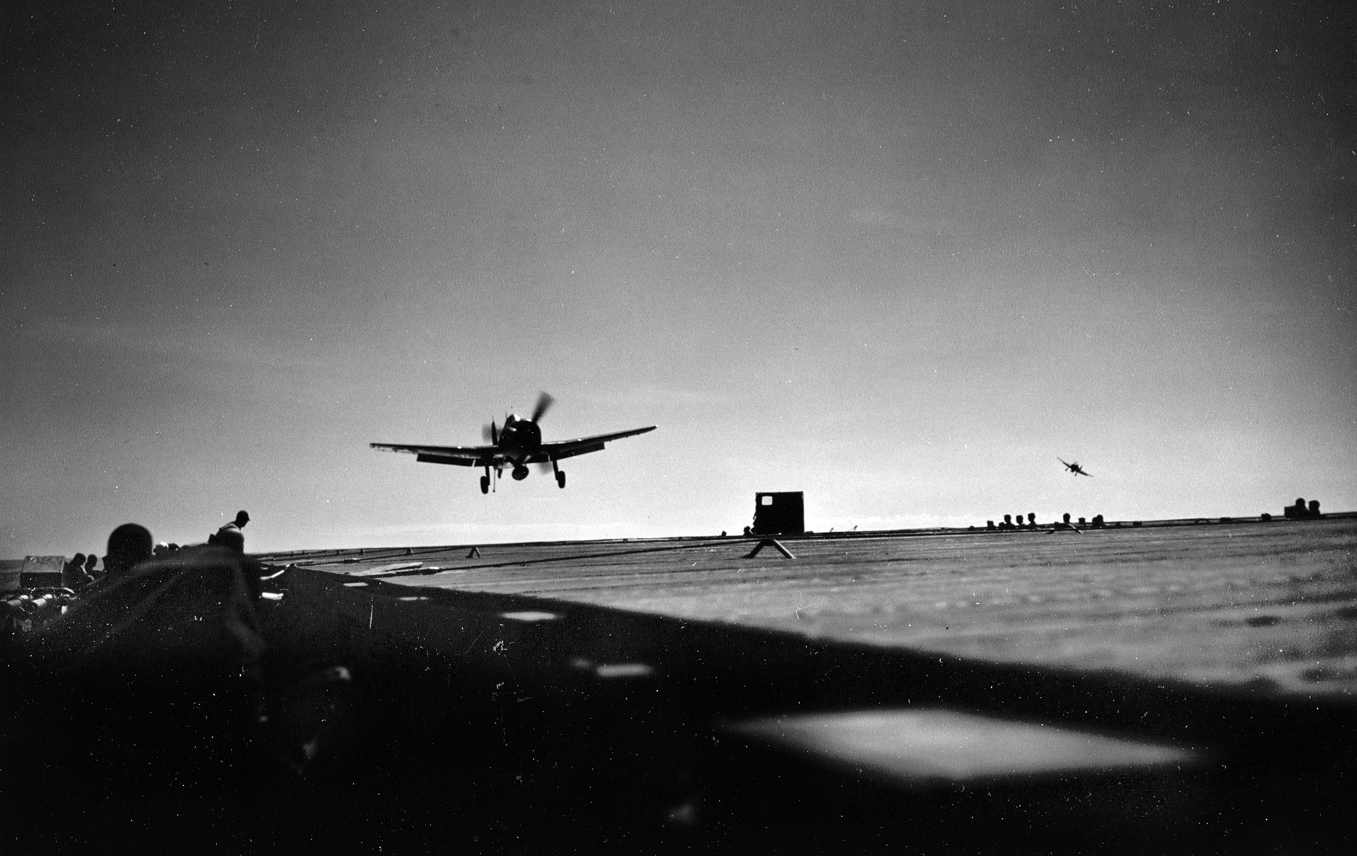 In the gathering darkness of early evening, a U.S. Navy Grumman F6F Hellcat fighter comes in for a landing aboard the aircraft carrier USS Cowpens.