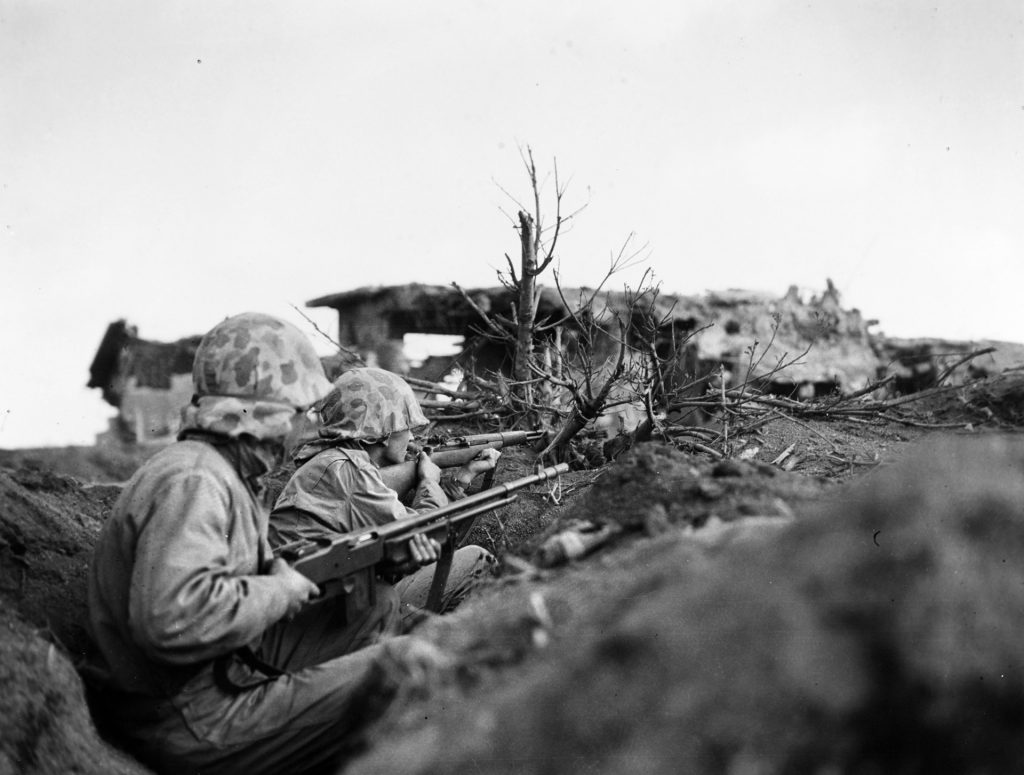Marines on Iwo Jima take cover from enemy fire near a captured Japanese pillbox. The island had been heavily fortified by the enemy and required 36 days of bitter combat before it was declared secured. INSET: By the time of the Iwo Jima landings, Marine Larry Kirby was a combat veteran.