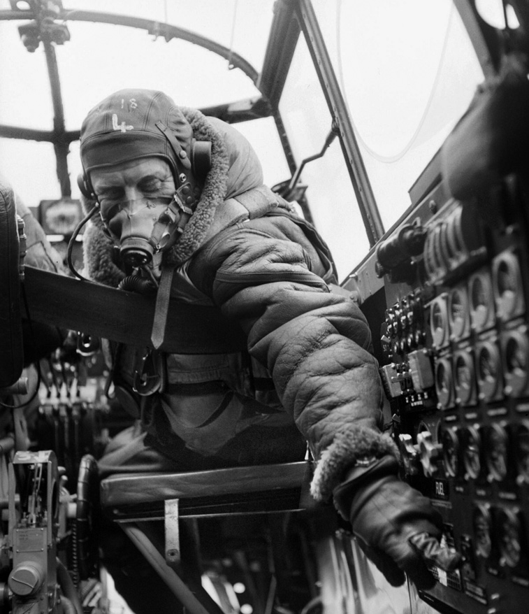 Checking instrument settings in the crew compartment of his Lancaster B Mk. III, a flight engineer prepares for a mission