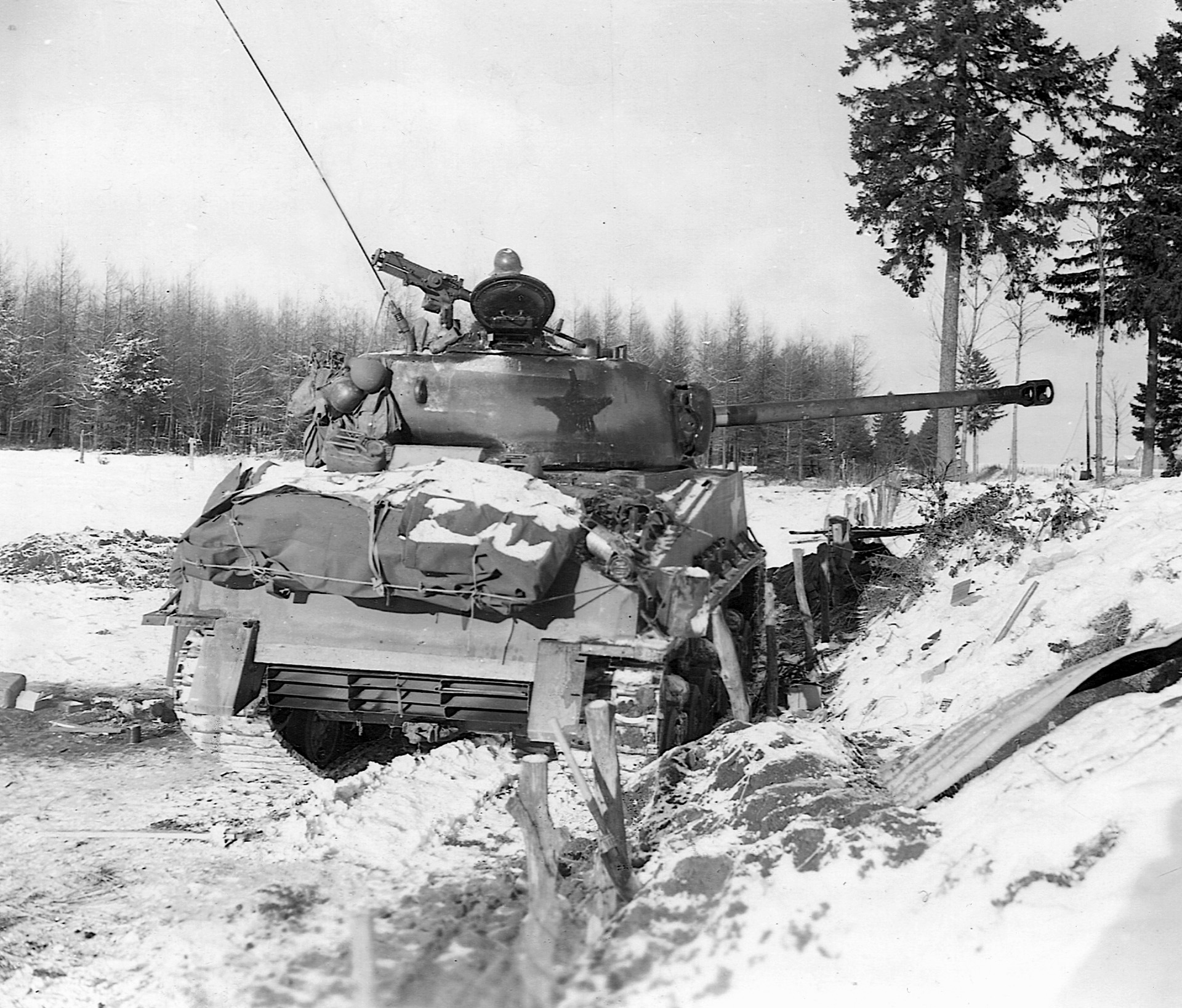  An M4 Sherman medium tank of the U.S. 4th Armored Division plows toward besieged Bastogne during the Battle of the Bulge in December 1944. The white star on the turret has been darkened to make it less visible to German troops.