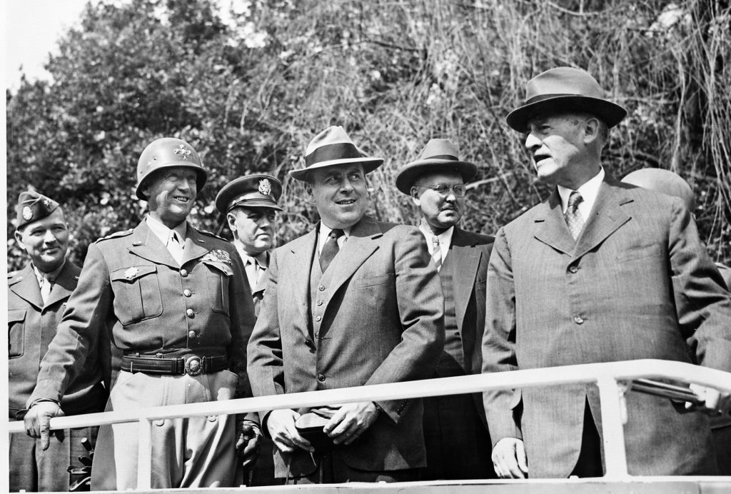 In July 1945, General Patton attends a gathering of senior military officers and civilian dignitaries in the German capital of Berlin. Secretary of War Henry L. Stimson stands at right.