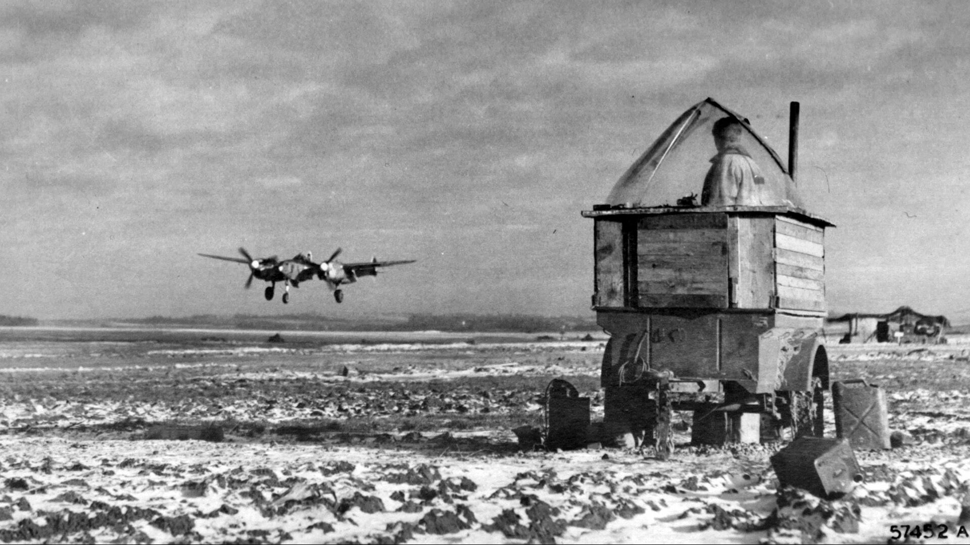 As a P-38 Lightning fighter of the 474th Fighter Group lands at a forward base in Belgium, the air tower on wheels in the foreground, with a ground crewman manning the post, is indicative of the mobile aspect of the Ninth Air Force. Tactical air support provided a critical element in the sustained advance of Allied ground forces into Germany. 