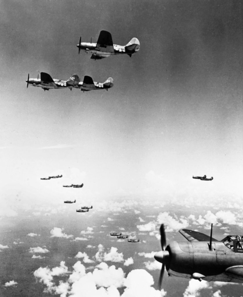 This photo was taken as American planes flew toward their targets, warships of the Imperial Japanese Navy, on June 20, 1944. The aircraft in the center background are Grumman TBF Avenger torpedo bombers. Those in the foreground are Curtiss SB2C Helldiver dive bombers.