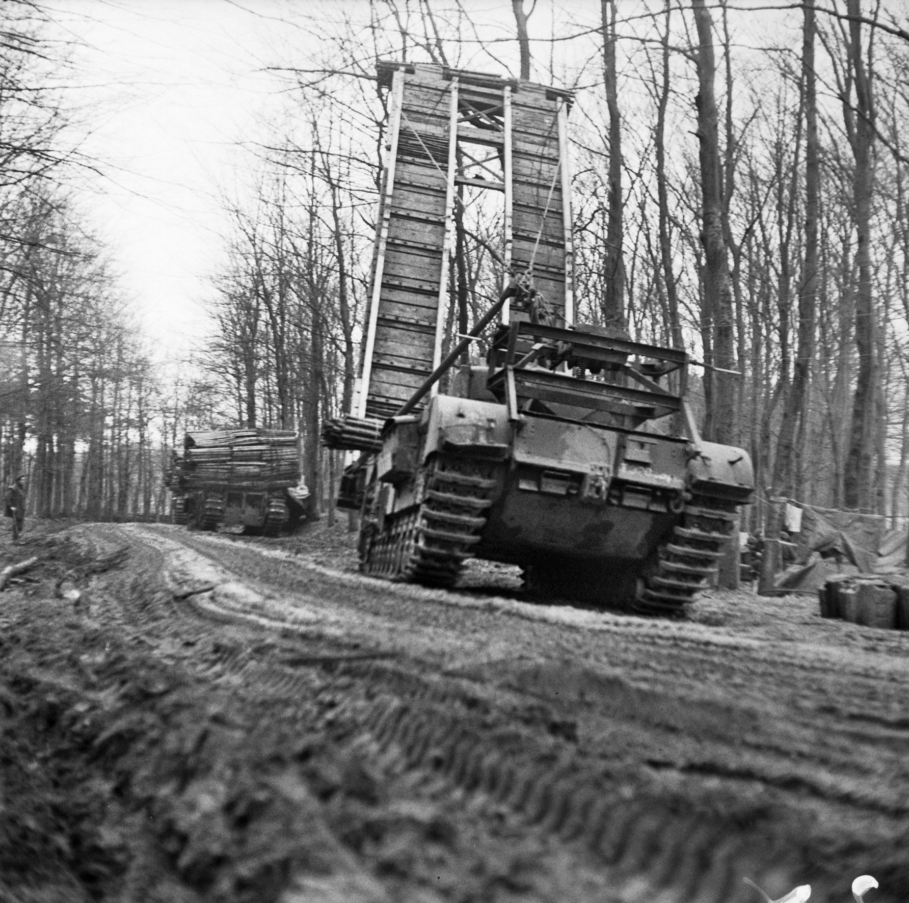 A British Churchill bridge-laying tank and another armored vehicle carrying fascines to be dropped into ditches to allow vehicles to cross ditches and other depressions in the ground follow the road toward the front during the Battle of the Reichswald.  