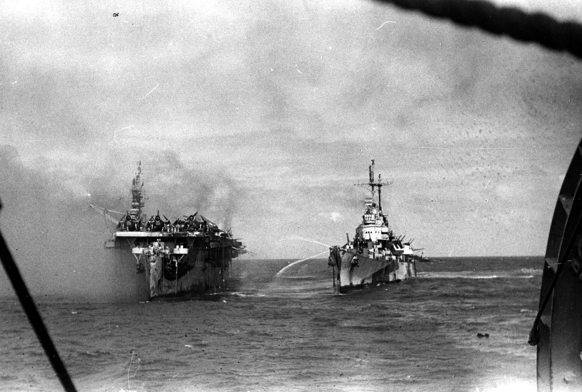 USS Birmingham attempts to train fire hoses along the port side of the Princeton. Moments later, an explosion ripped through the carrier and badly damaged the cruiser as well.
