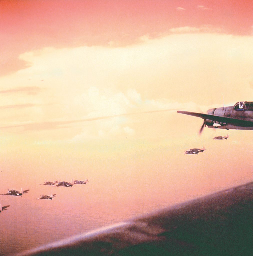 Curtiss Helldiver bombers from the USS Intrepid fly over Filipino airspace as the sun sets to the east. 