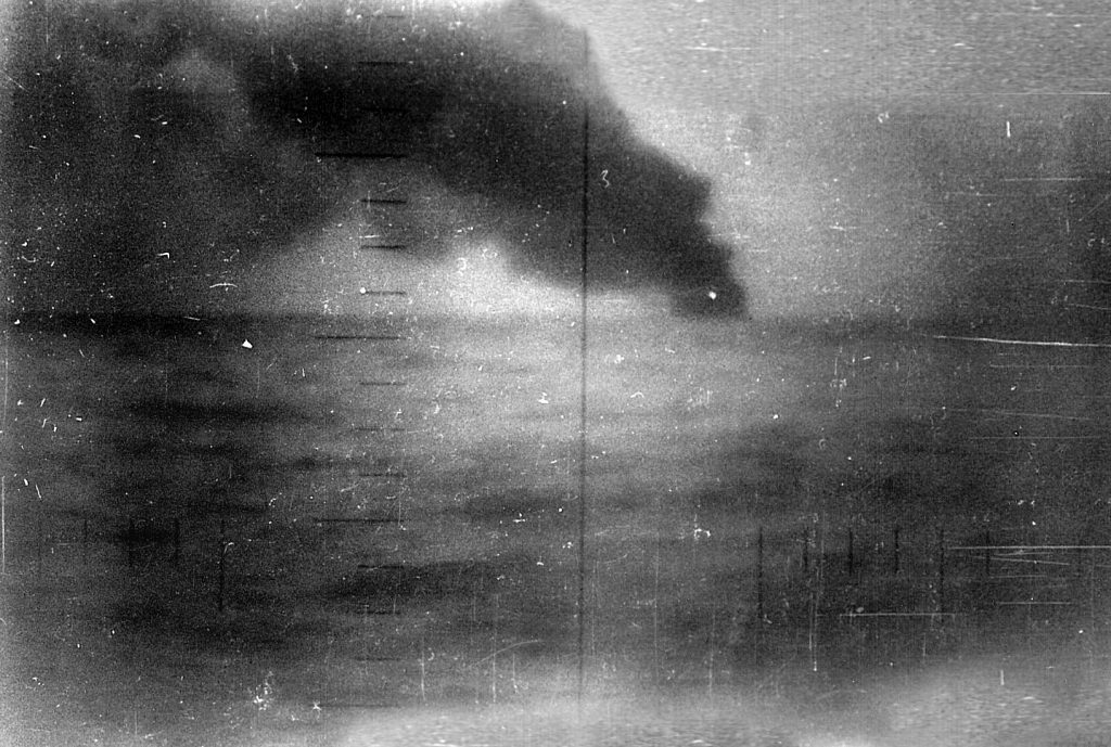 Seen through the periscope of the U.S. Navy submarine that has just successfully attacked it, a stricken Japanese warship lists to port and belches a heavy cloud of black smoke before plunging to the bottom off the coast of the Philippines. 