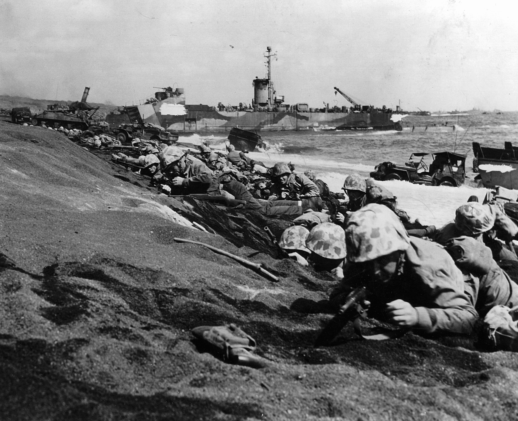 Taking cover from interlocking fields of Japanese mortar, artillery, and small arms fire, troops of the 4th Marine Division lay low on the beach at Iwo Jima. 