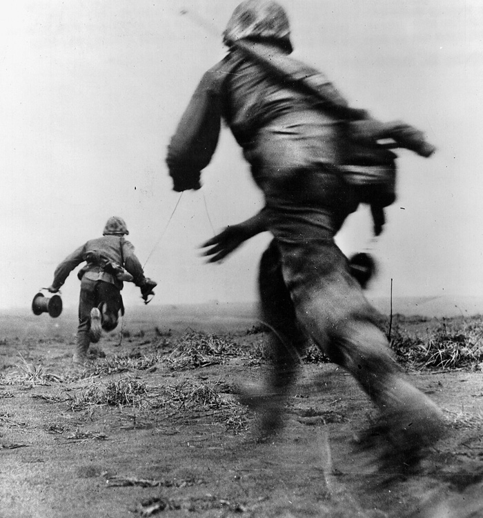 In an effort to establish field contact with the front lines, two Marine wiremen race across an open field under enemy fire.
