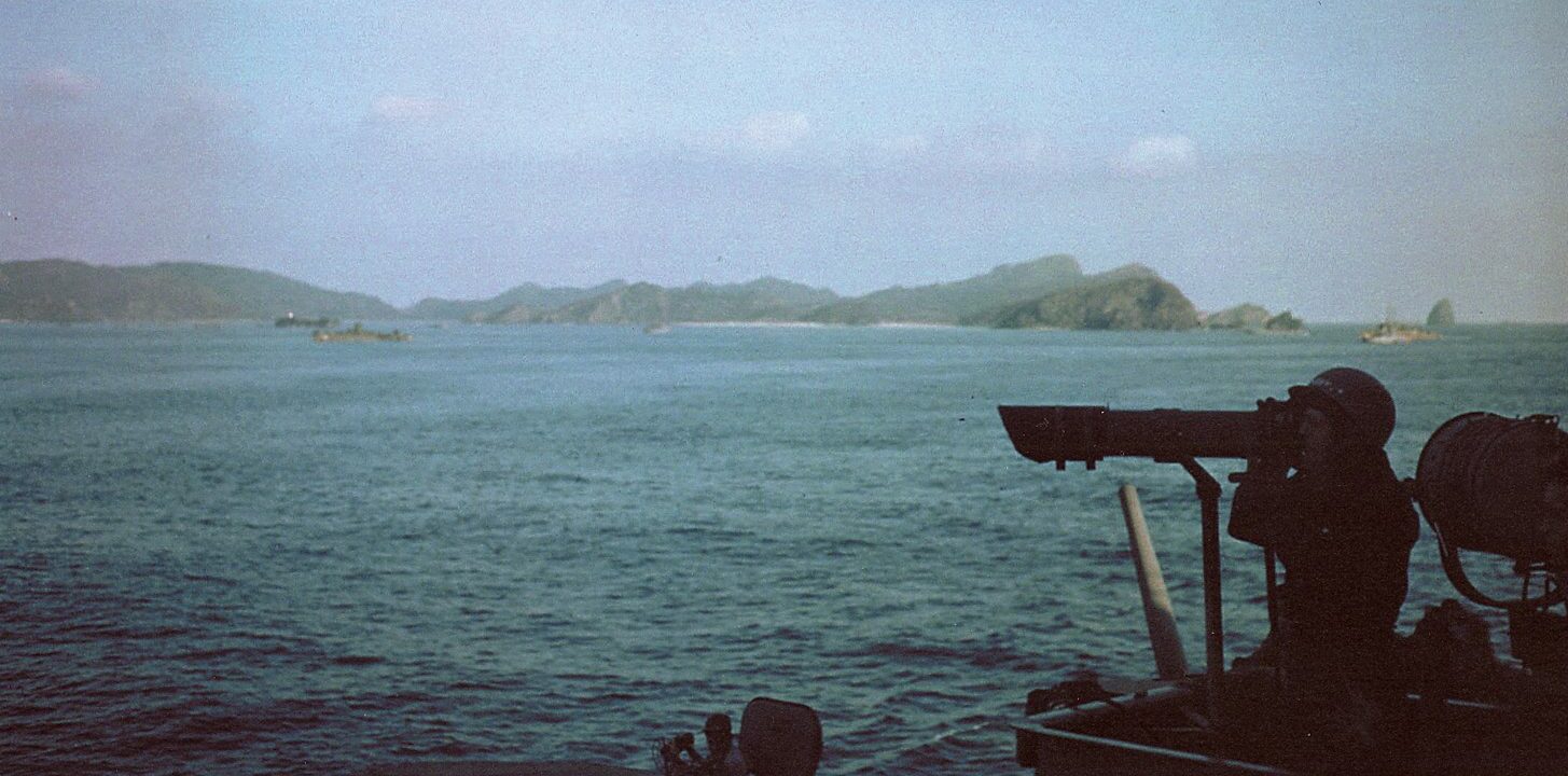 An artillery spotter carefully examines the island shoreline. 