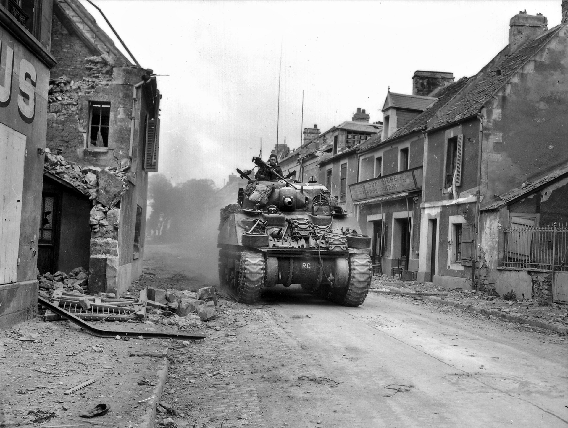 A Sherman tank from the Canadian 27th Tank Regiment rolls through the shattered, deserted streets of Caen after the Germans pulled out. The British/Canadians lost thousands of men and 300-500 tanks. The delay in securing Caen badly damaged Montgomery’s reputation among the Allies.