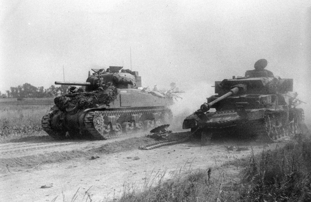 A Lend-Lease Sherman tank belonging to a British unit kicks up dust as it speeds past a knocked-out PzKpfw IV near Gagny on July 19, 1944.